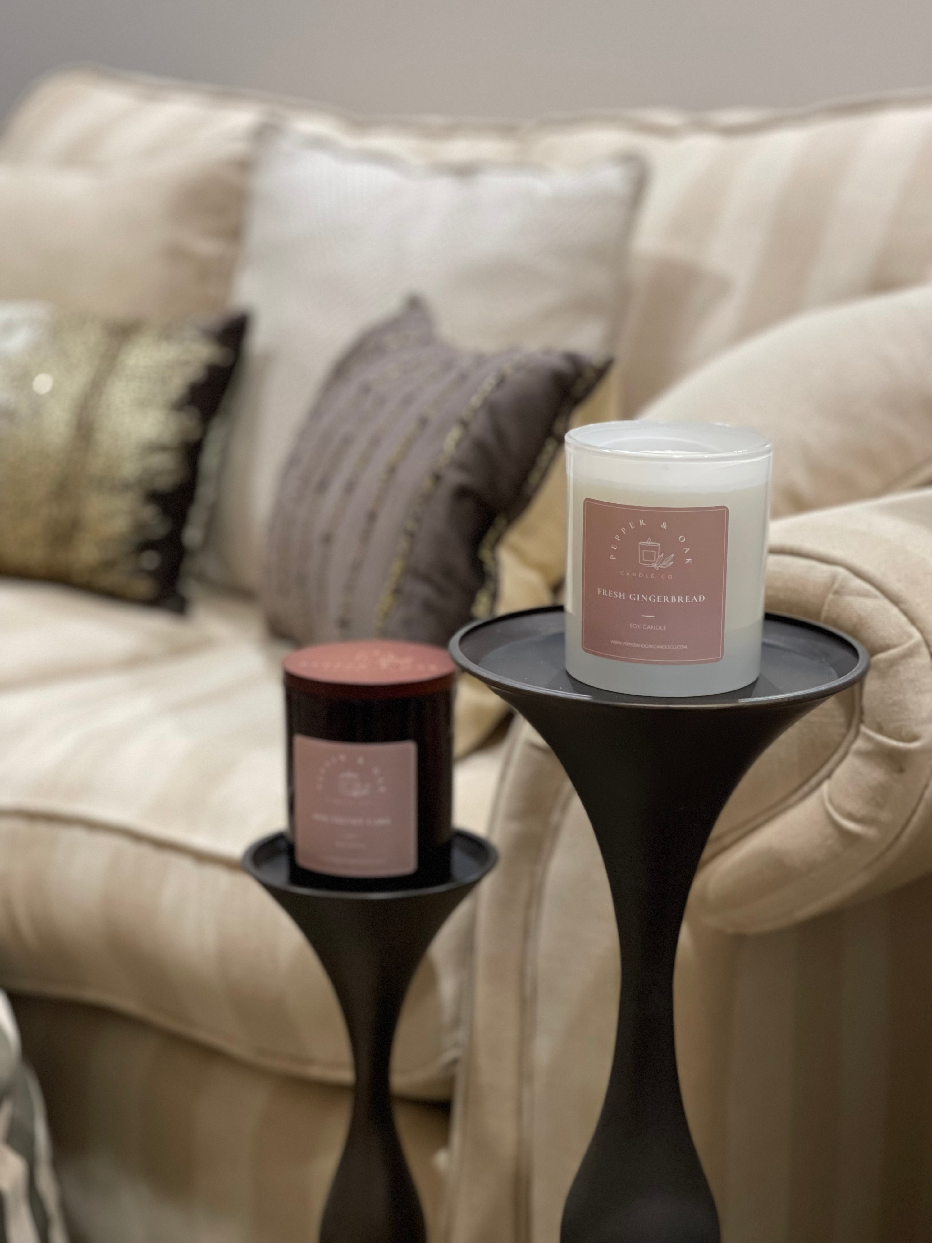 Two large soy candles on stands in a grand lounge room with plush fabric couch