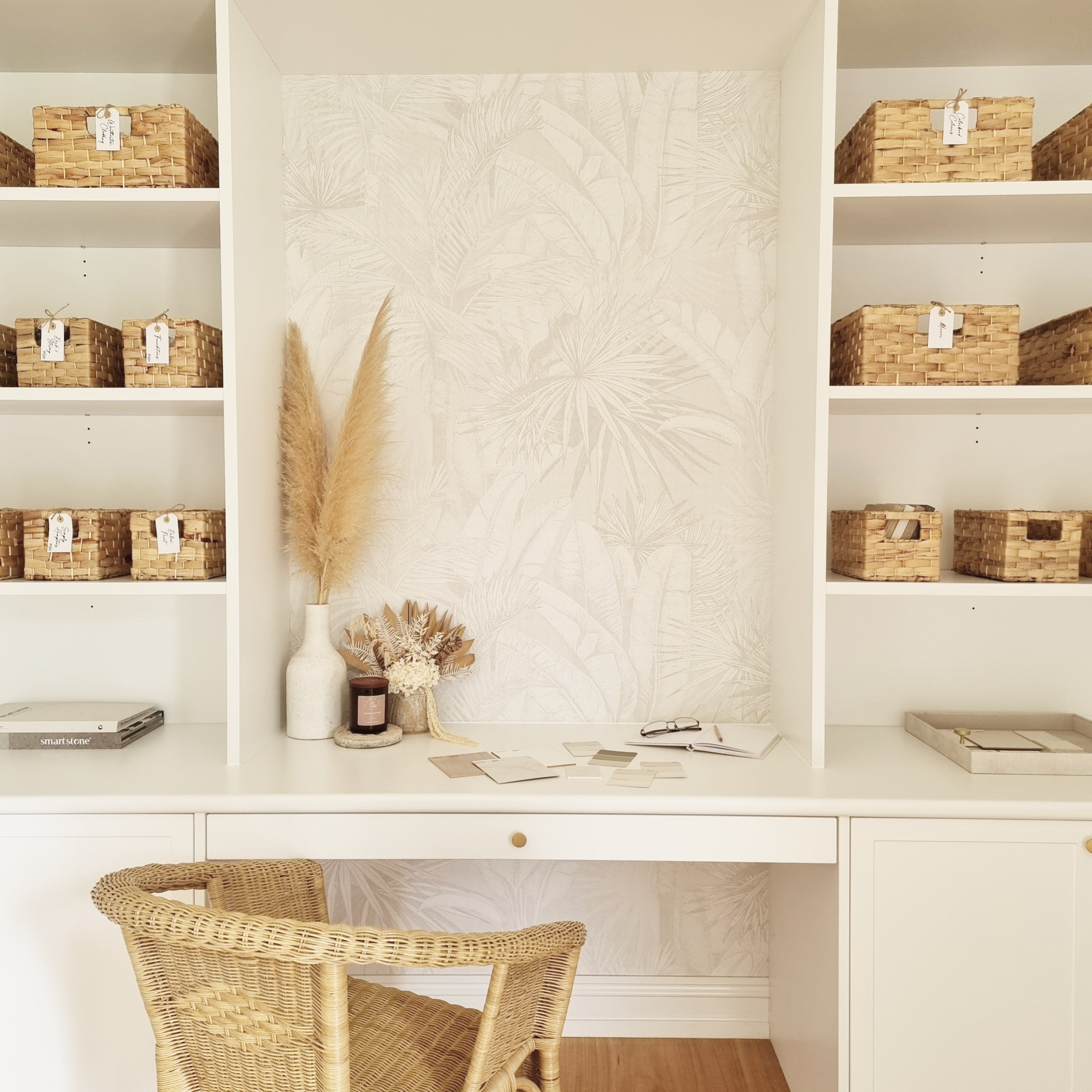 A candle on a desk in a very organised study placed next to dried flower arrangements 