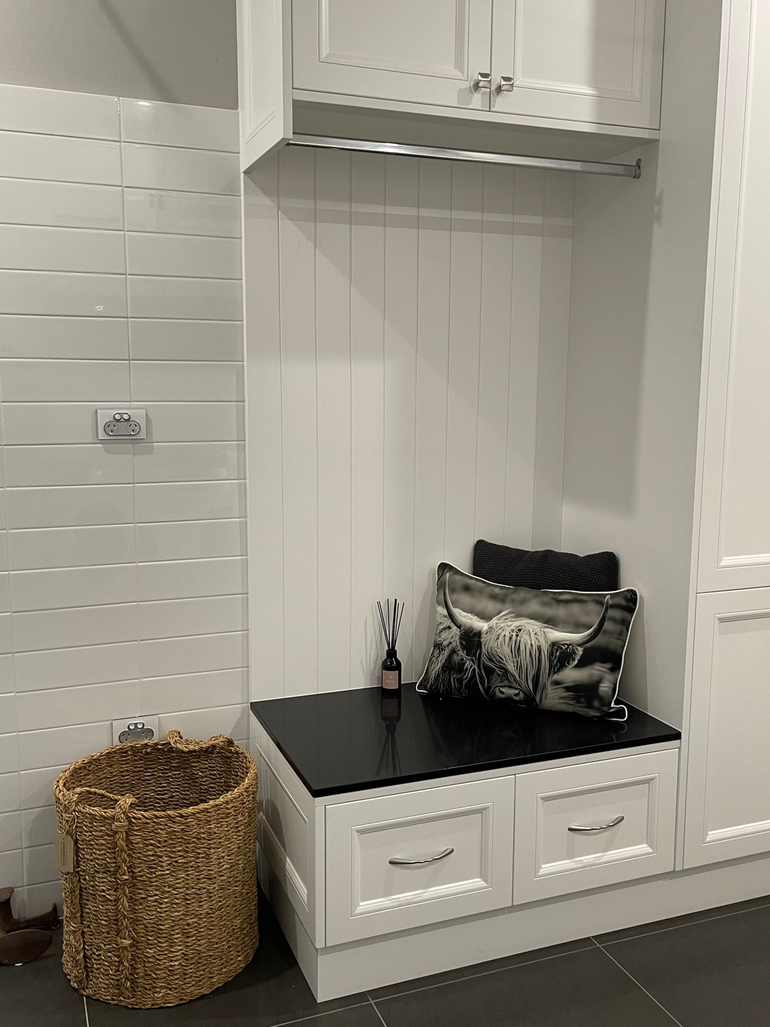 A reed diffuser sitting on a bench in a white laundry next to a pillow of a highland cow