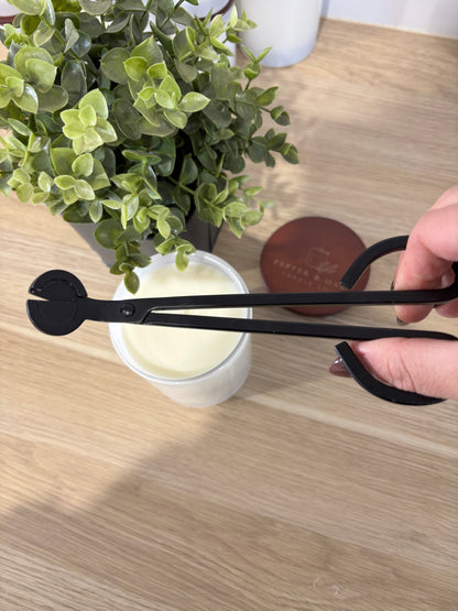 Black wick trimming scissors held over a plant and container on a wooden surface.